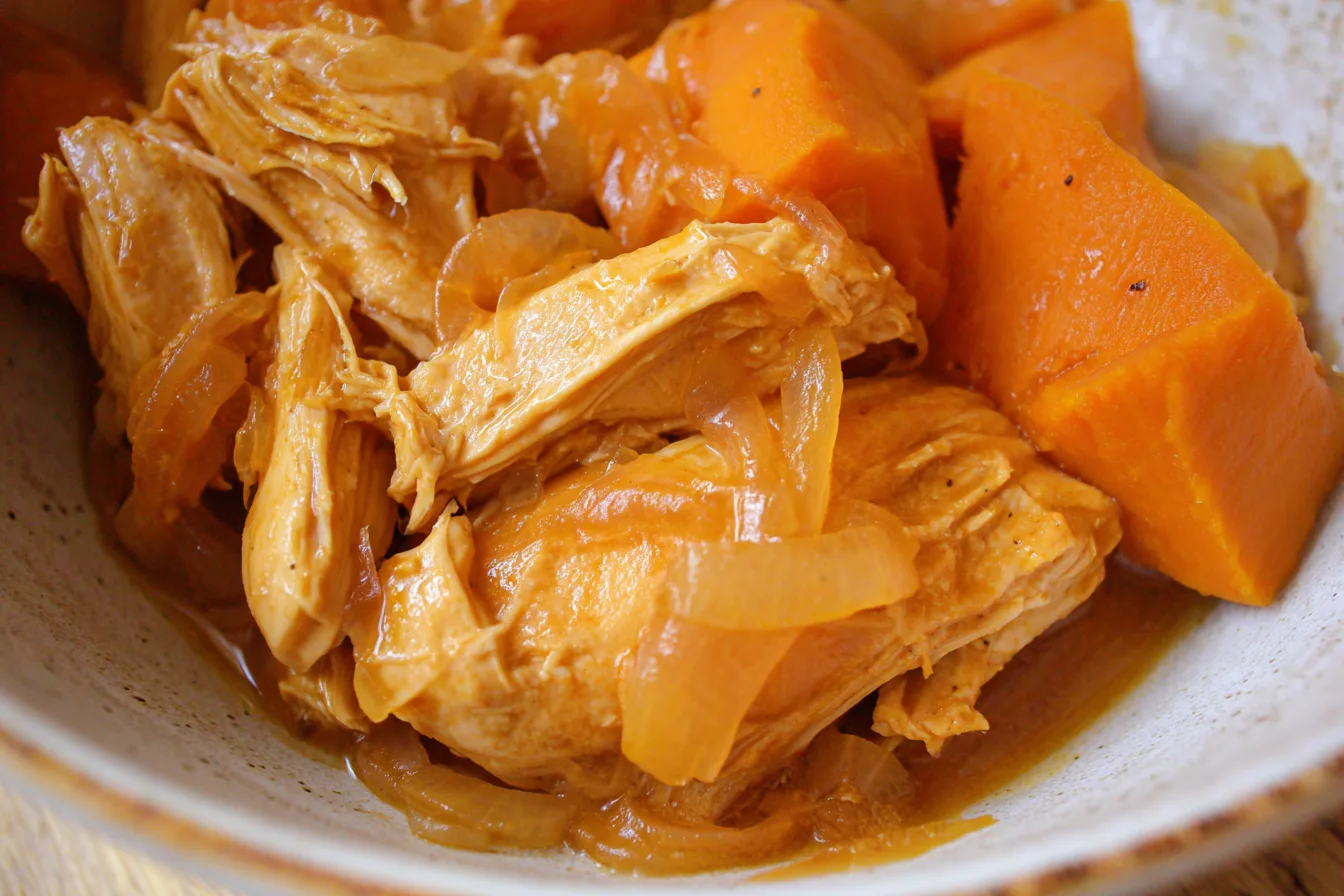 Shredded maple Dijon chicken with sweet potato chunks and onions in a ceramic bowl.