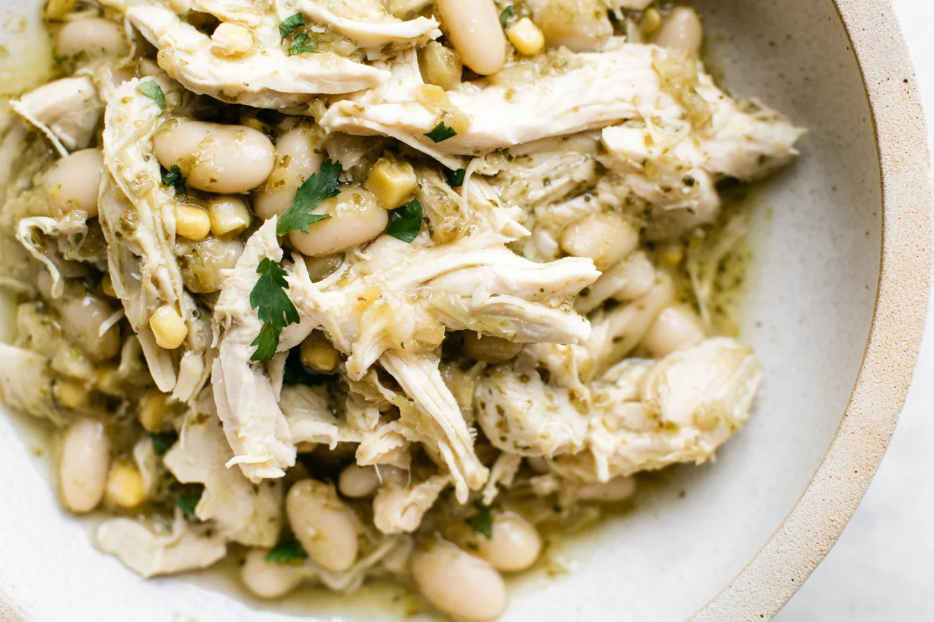Close-up bowl of shredded salsa verde chicken with white beans, corn, and cilantro.