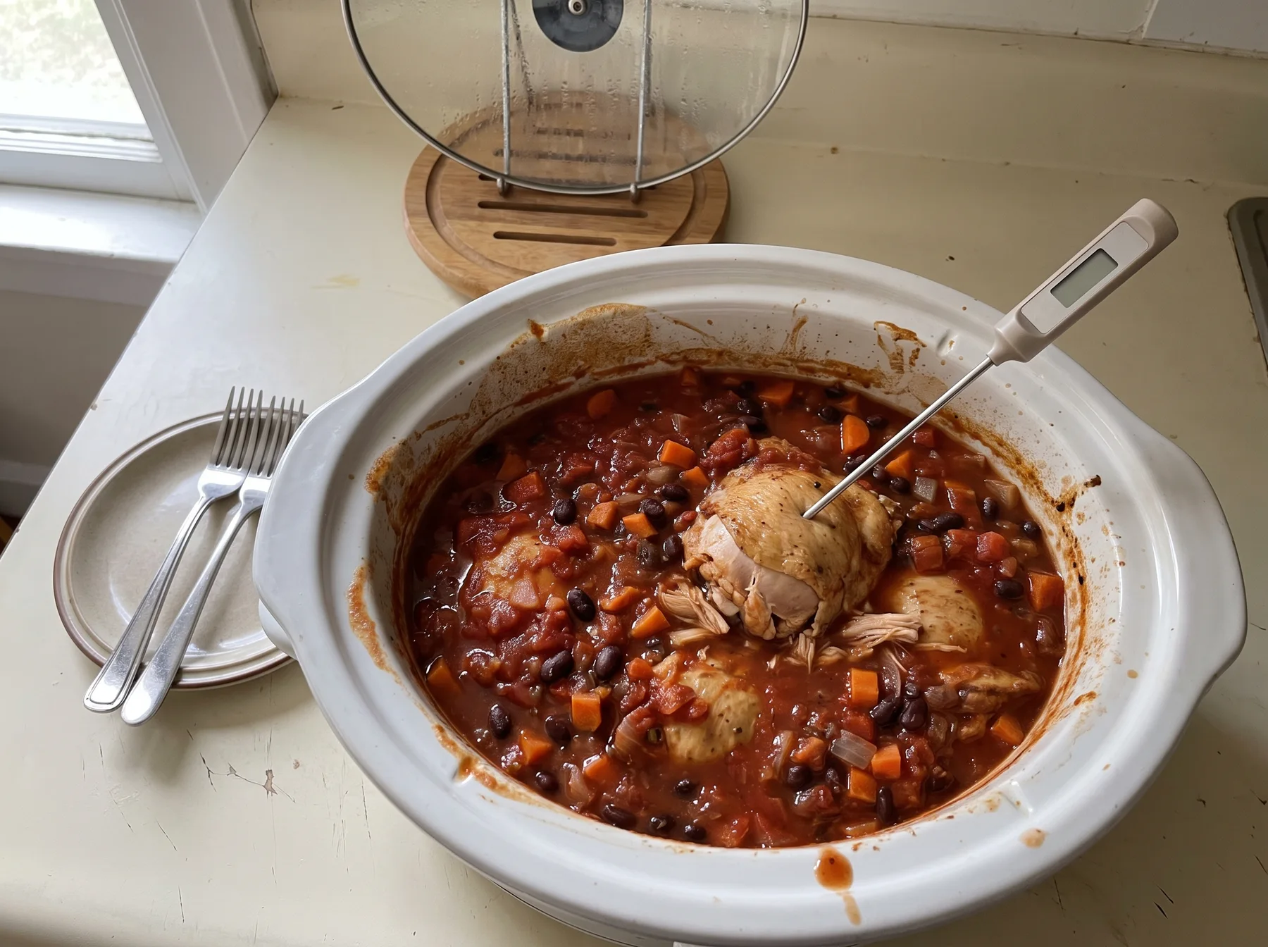 Food thermometer inserted into cooked chicken in a slow cooker with beans and tomato sauce.