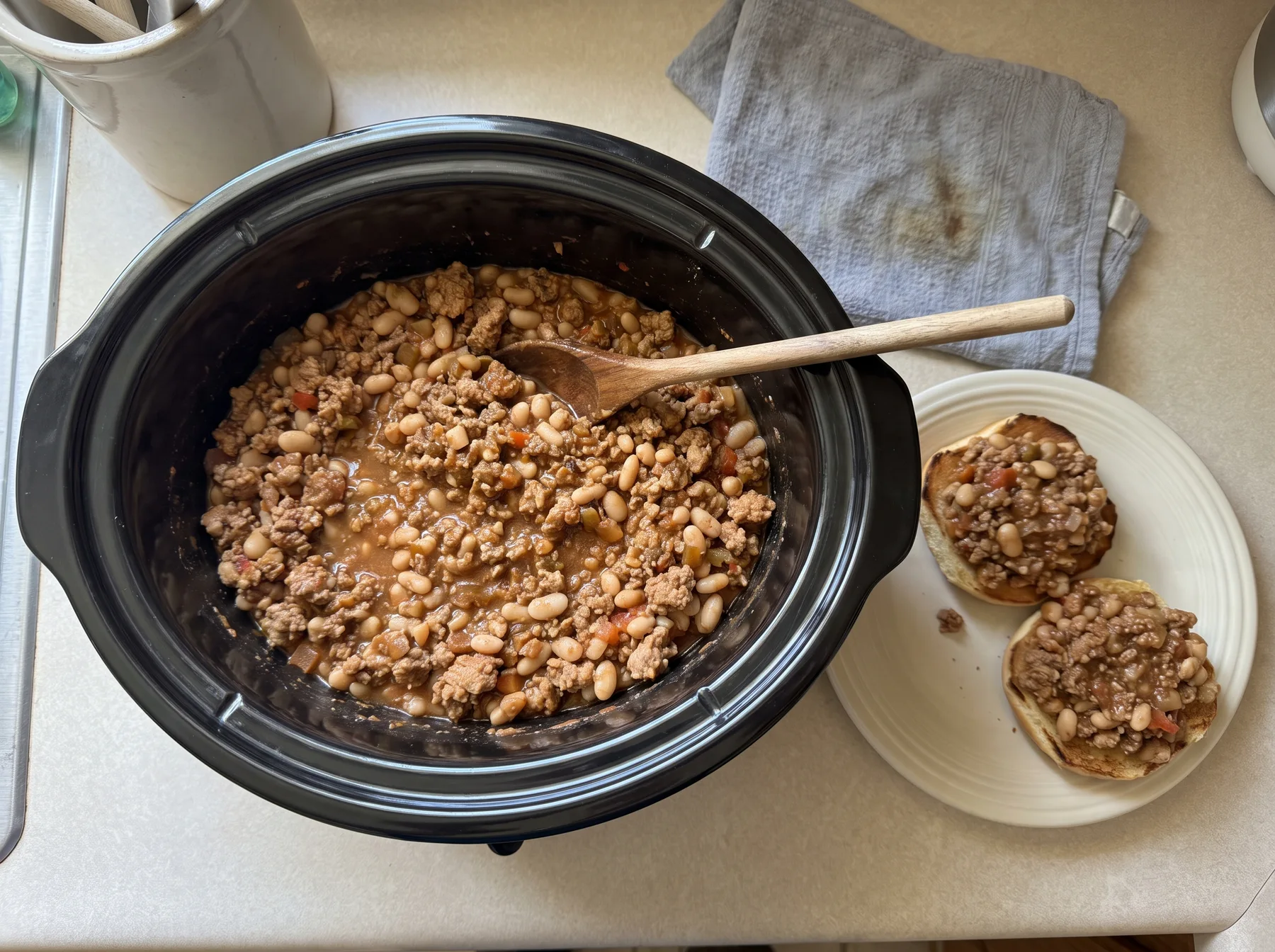 Turkey and white bean sloppy joe filling in a slow cooker beside two open sandwiches.