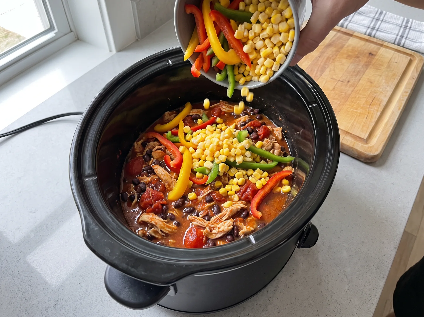 Corn and sliced peppers are poured into a slow cooker with shredded chicken and beans.